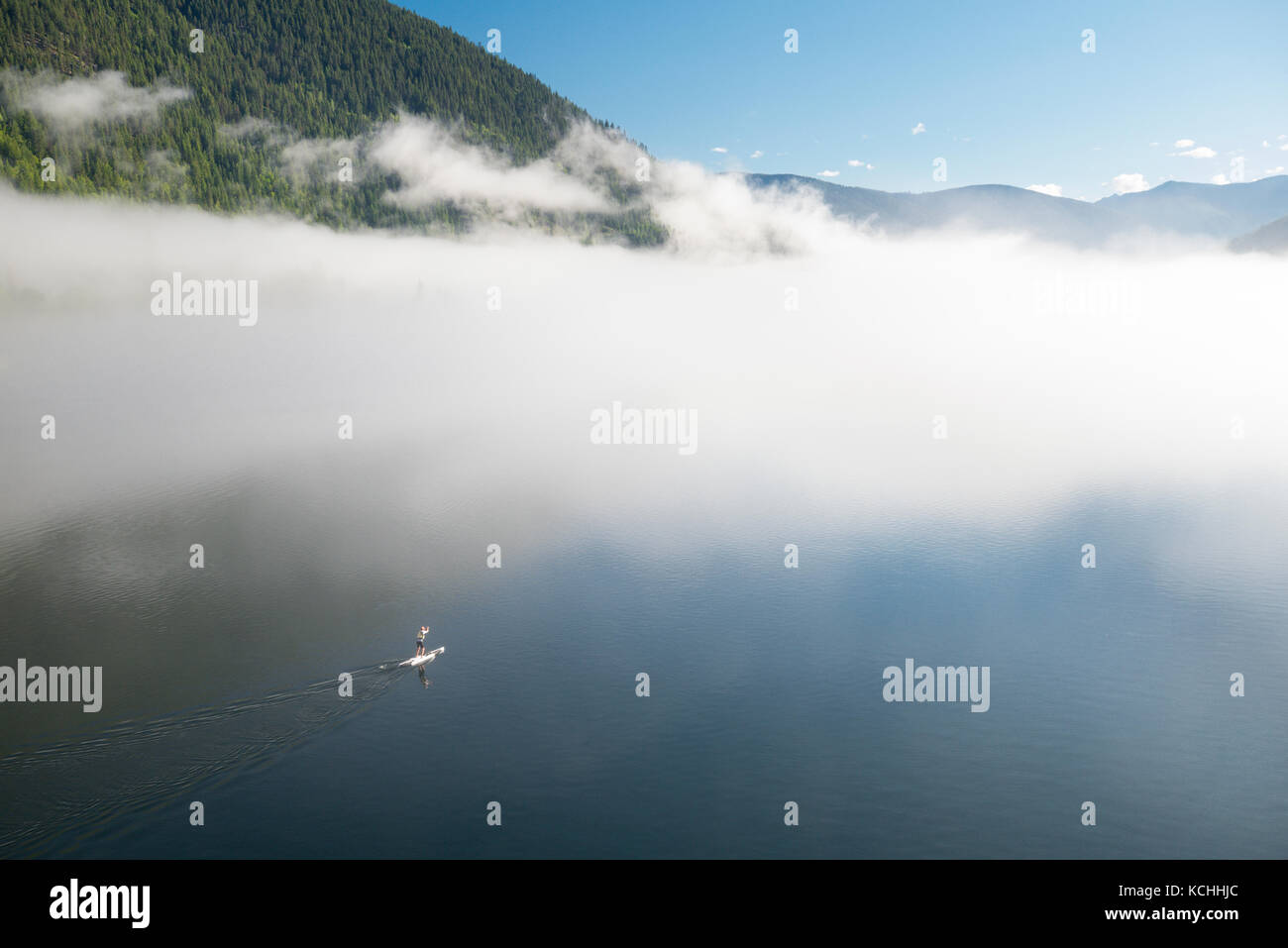 Un stand-up tele paddleboarder acque di nebbia-laden Kootenay Lake in Nelson, British Columbia Foto Stock
