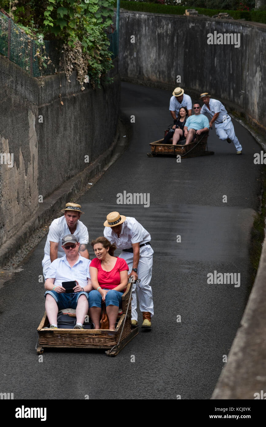 I turisti scivolare giù per la collina di traditiopnal cesto in vimini toboga a monte vicino a Funchal in Madeira Foto Stock