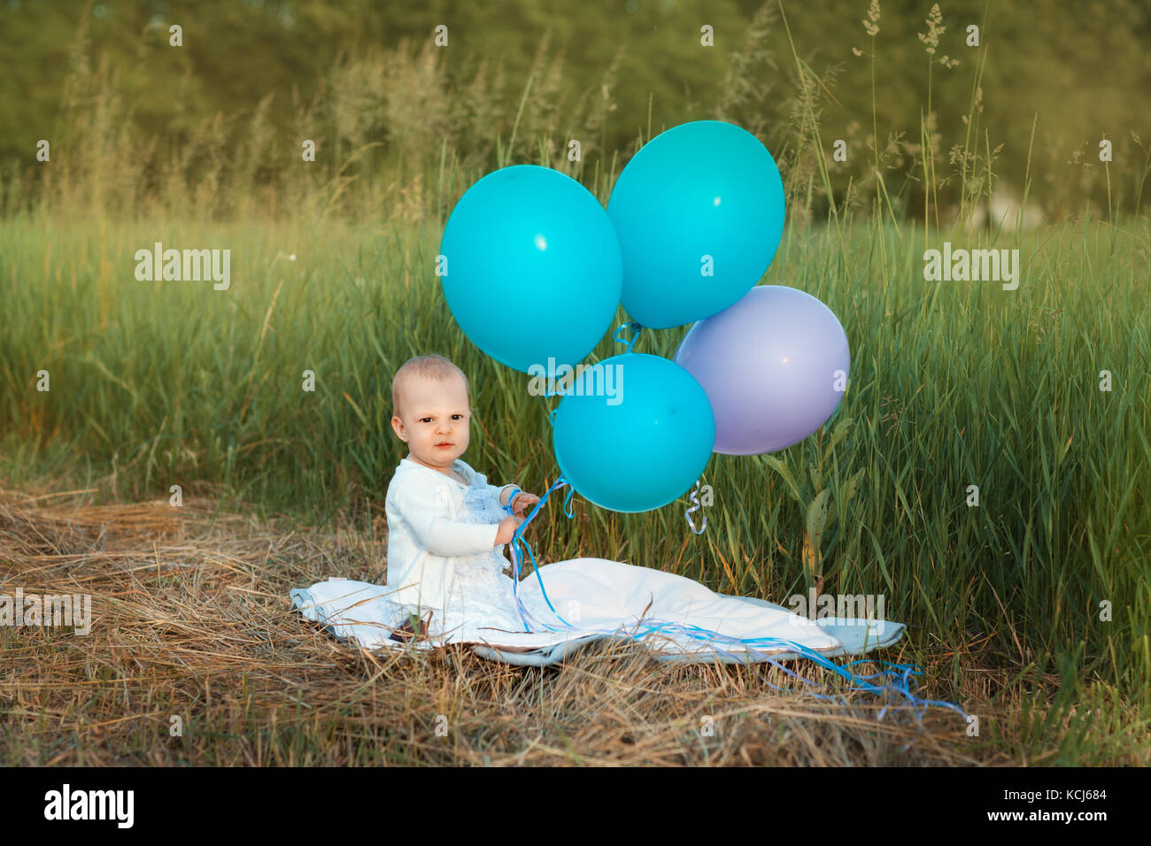 Baby ragazza seduta in erba e palloncini di contenimento Foto Stock