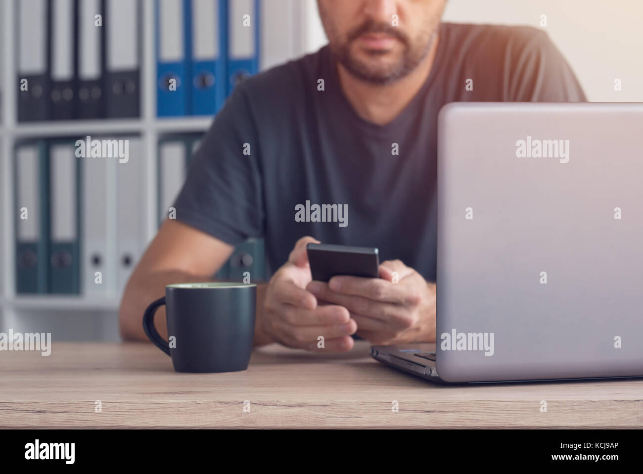 Libero professionista sms sul cellulare dalla sua scrivania in ufficio in casa Foto Stock