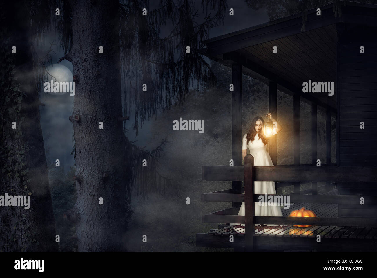 Spooky ragazza in un abito bianco, tenendo in mano una lanterna accesa, una zucca vicino a lei, sul balcone di una casa in legno, in una scura foresta di nebbia, sotto la luna. Foto Stock