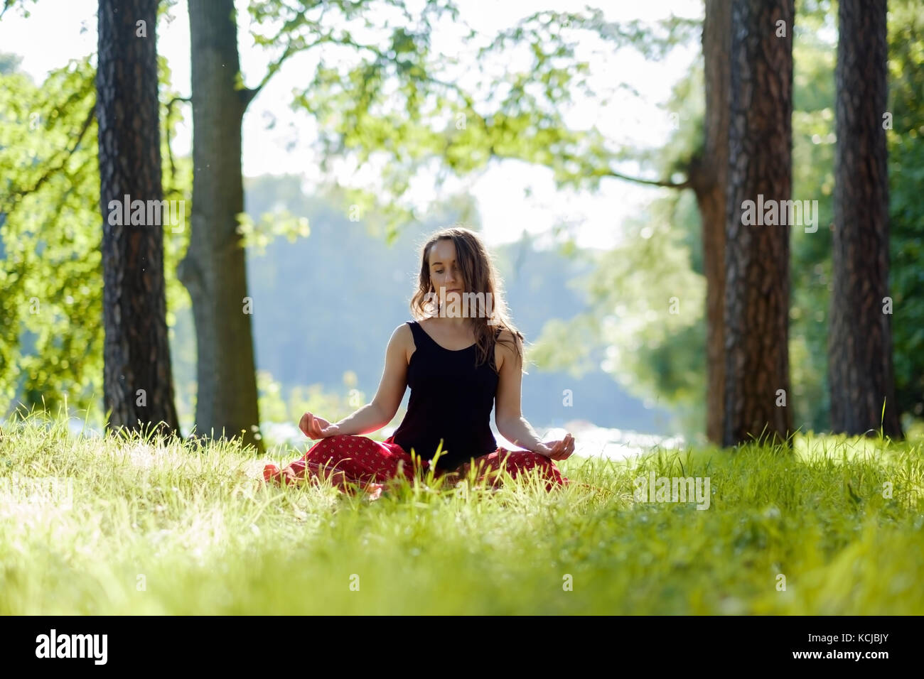 Giovane donna in gonna rossa godendo di meditazione e yoga su erba verde in estate sulla natura Foto Stock