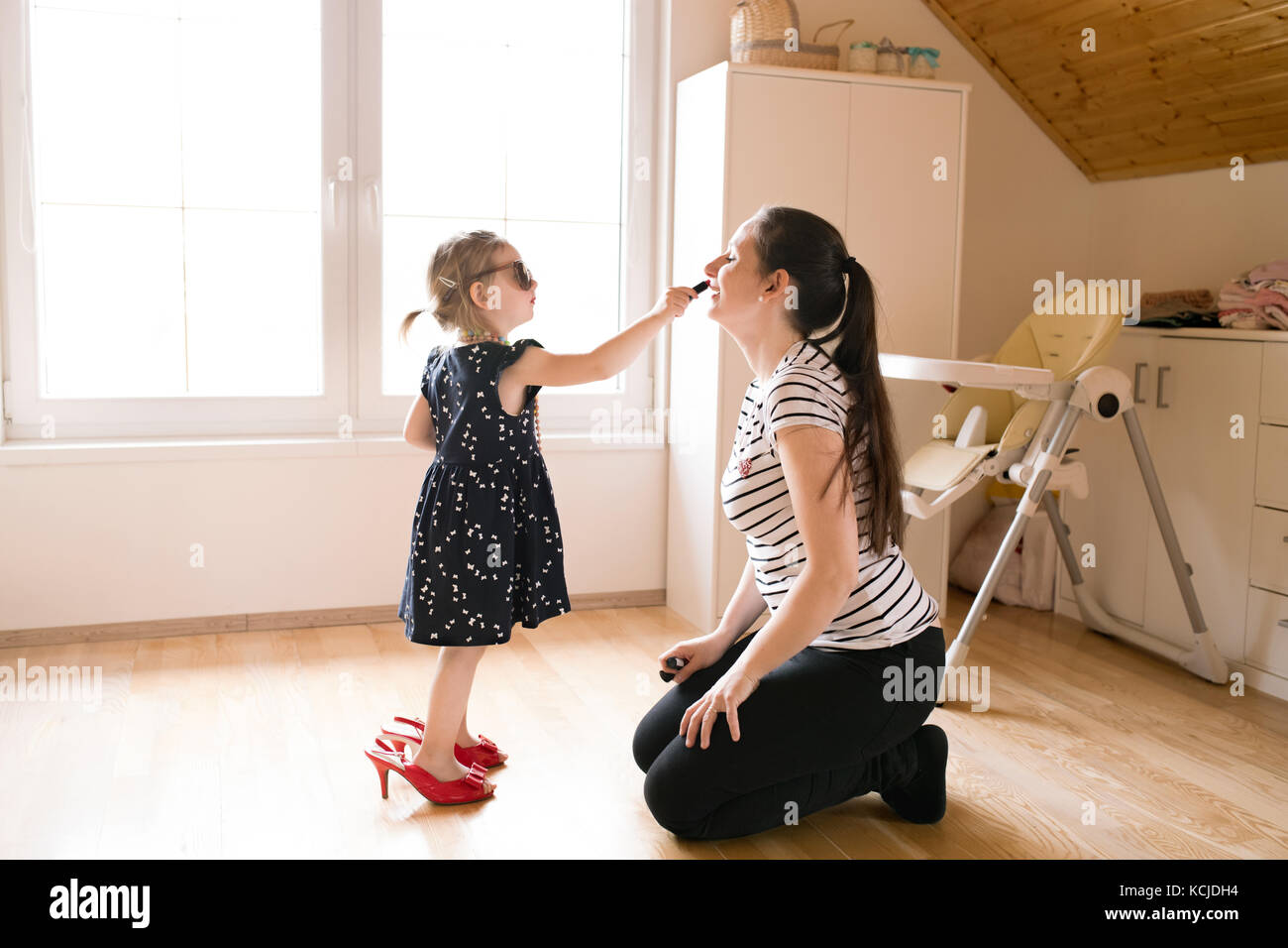 Bambina facendo il make-up per il suo attraente madre con il rossetto Foto Stock