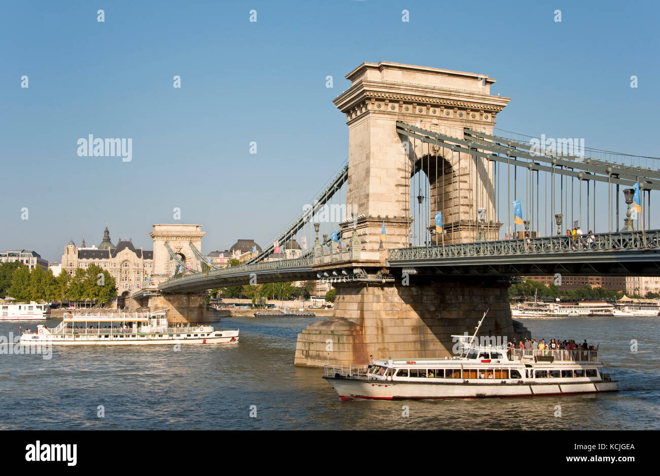 Una vista del Ponte delle catene Széchenyi a Budapest con una gita di un giorno in barca fluviale che passa sotto in una giornata soleggiata con cielo blu. Foto Stock
