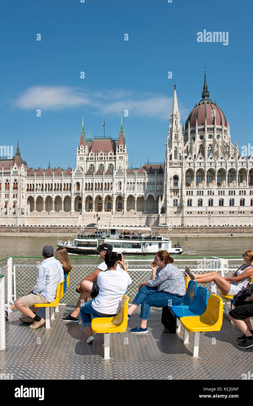 I turisti che amano una crociera sul Danubio passano accanto al Palazzo del Parlimento Ungherese in una giornata soleggiata con il cielo blu. Foto Stock