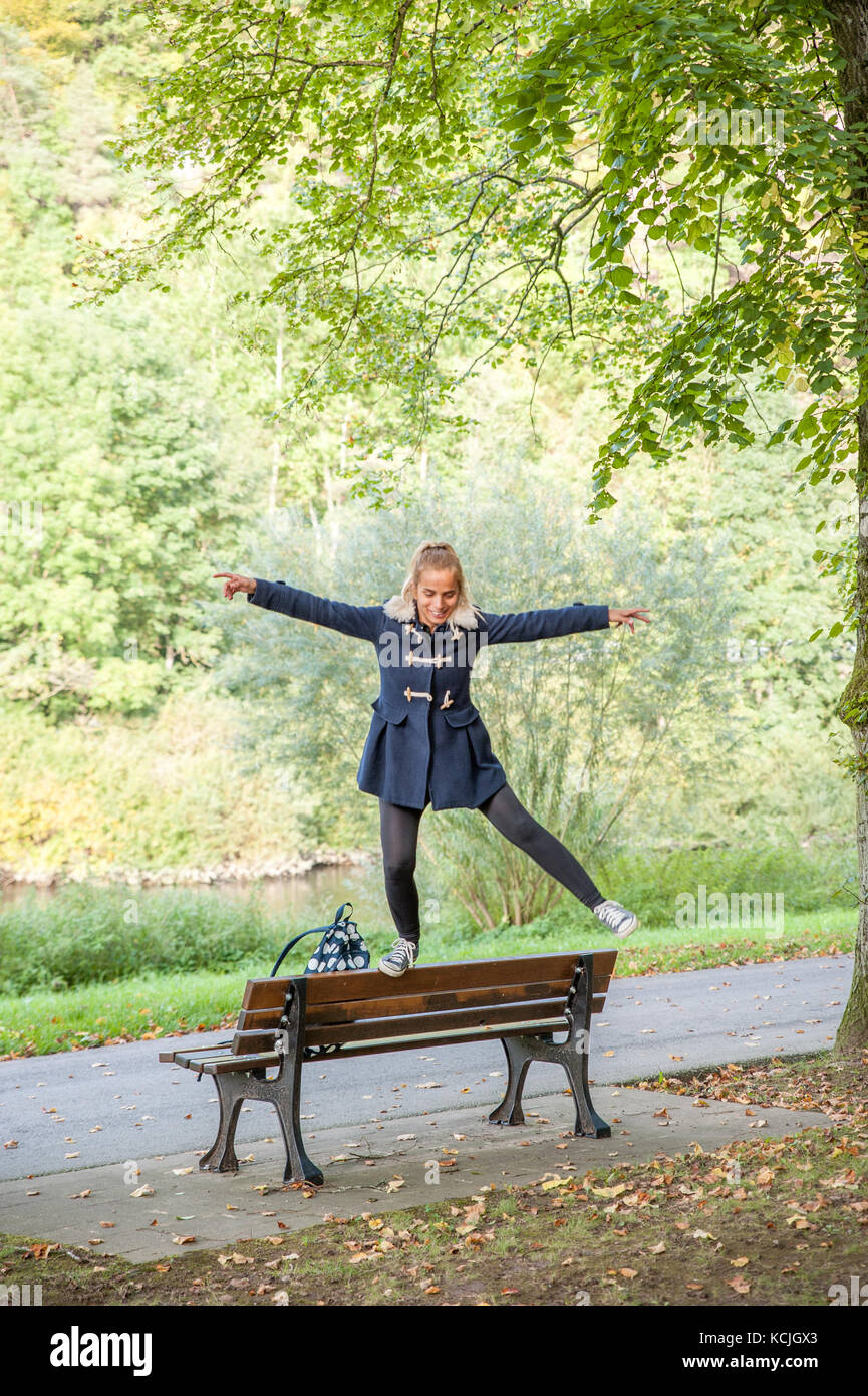 Giovane donna salta sopra il banco di legno in un parco pubblico, Lussemburgo Foto Stock