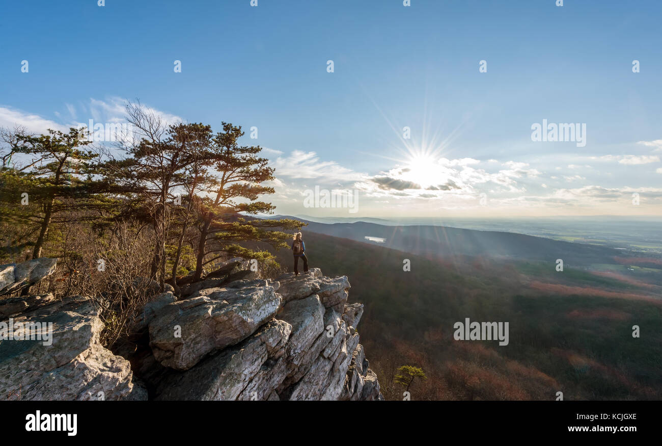 Escursionista femmina in piedi nel vento in corrispondenza di un bordo di una scogliera rocciosa sulla cima di una montagna appalachian godendo del tramonto e vista Foto Stock