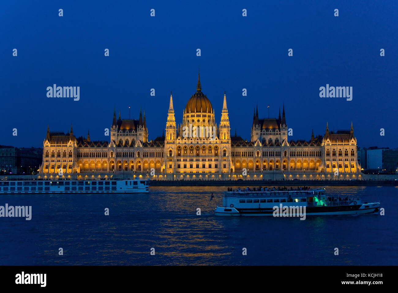 Una vista notturna dell'edificio del Parlimento Ungherese sul Danubio a Budapest con una nave da crociera turistica sul fiume che passa. Foto Stock