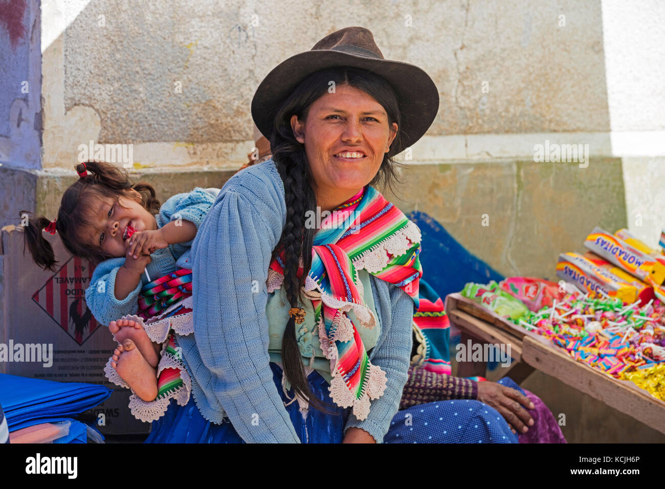 Cholita, donna boliviana con cappello e treccia lunga nera dei capelli che porta bambino sulla sua schiena nella città di Tarabuco, Chuquisaca, provincia di Yamparáez, Bolivia Foto Stock