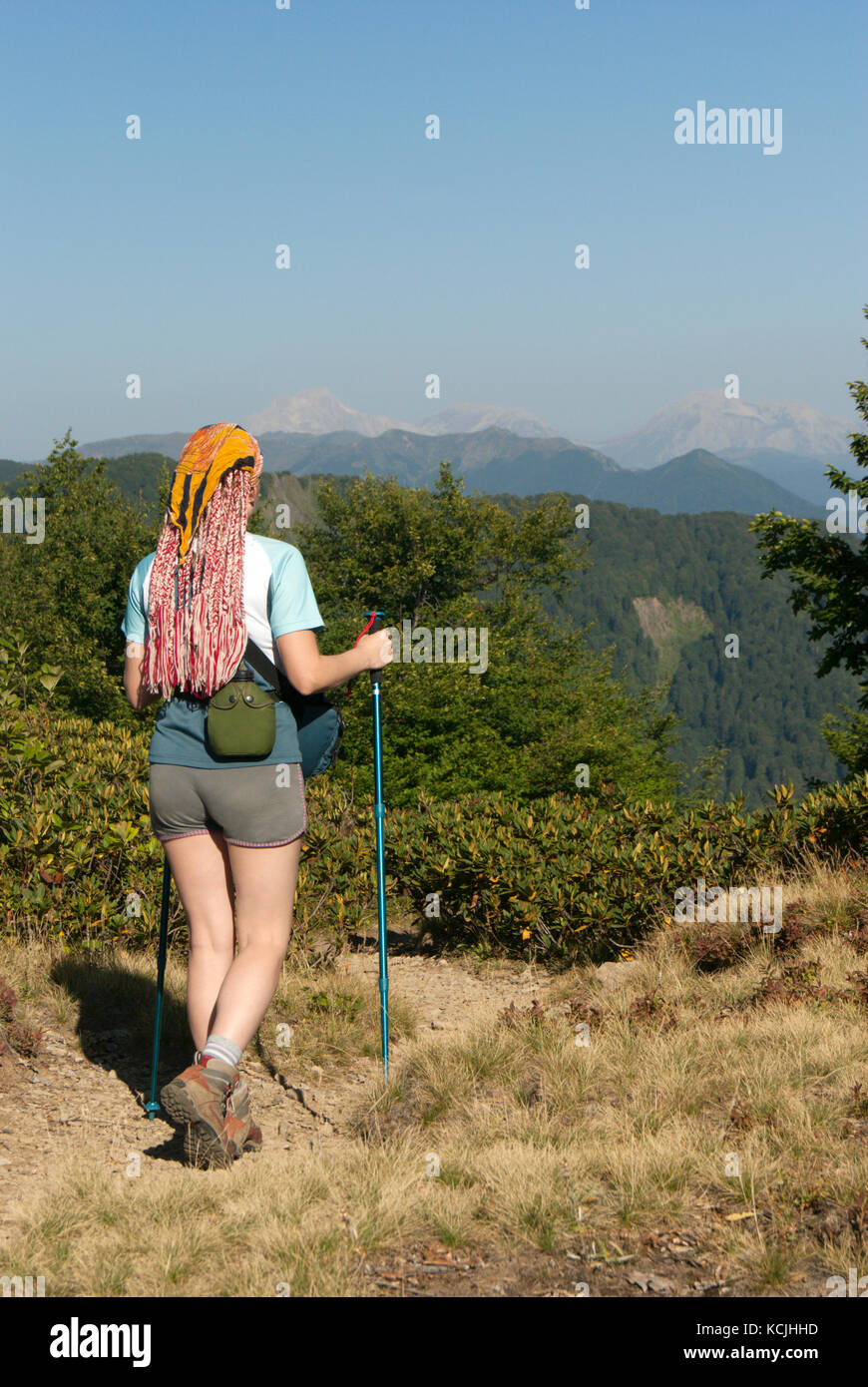 Una ragazza con i bastoncini per la camminata nordica, pallone per acqua e una borsa per macchina fotografica a piedi lungo un sentiero di montagna contro lo sfondo delle vette nel Foto Stock