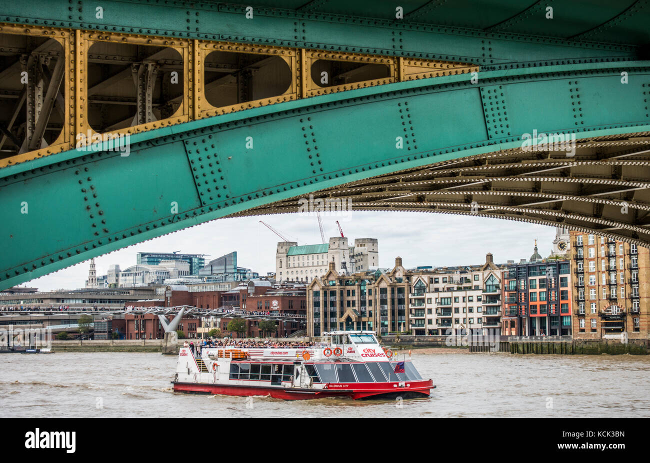 Sezione arcuata di Southwark Bridge sul Bankside, con una crociera di occupato passando in barca sul fiume Tamigi e il Riverside edifici, Londra, Inghilterra, Regno Unito. Foto Stock