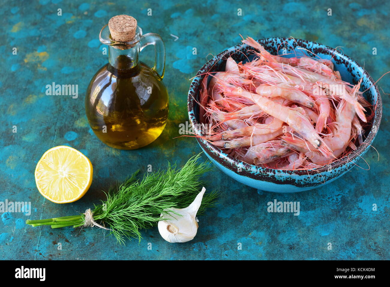 Materie gamberi in una tradizionale greco per la coppa con olio di oliva jar, sale marino, limone rosmarino su un sfondo astratto. Il mangiare sano concetto Foto Stock