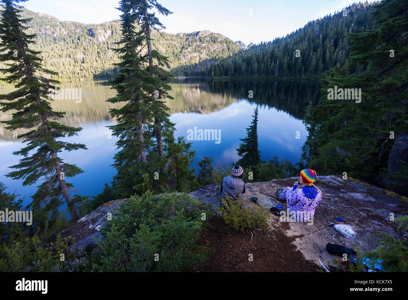 Due amiche, che si accamparano al lago Bedwell, gustatevi un caffè di prima mattina. Strathcona Park, Central Vancouver Island, British Columbia, Canada Foto Stock