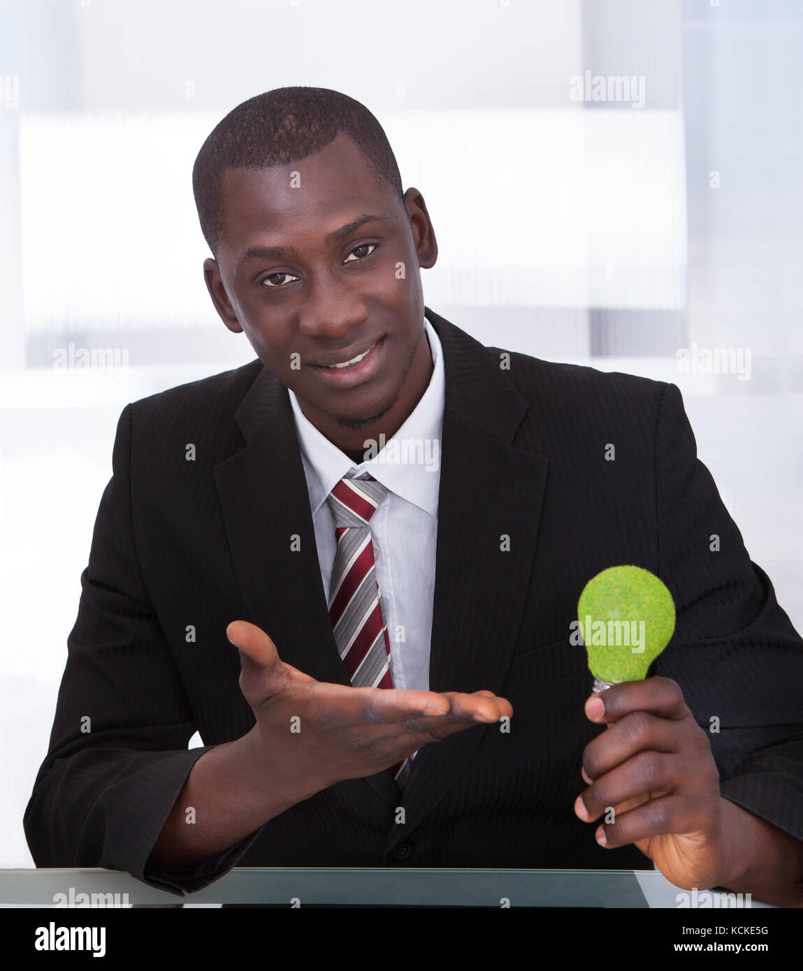 Ritratto di un uomo d'affari africani holding lampadina ecologica in ufficio Foto Stock