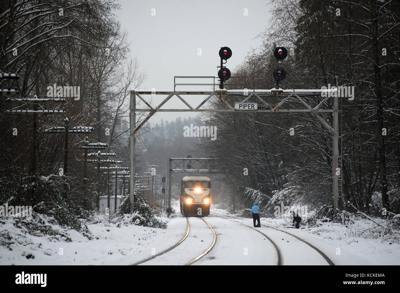Lavoratori chiaro di neve da un interruttore via come un Amtrak Cascades treno attende, Burnaby, British Columbia, Canada. Foto Stock