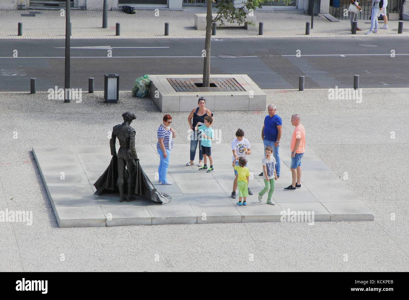Famiglia di turisti riuniti intorno alla statua del matador Christian Montcouquiol ('Nimeño II') di fronte all'Arena di Nimes, un anfiteatro romano Foto Stock