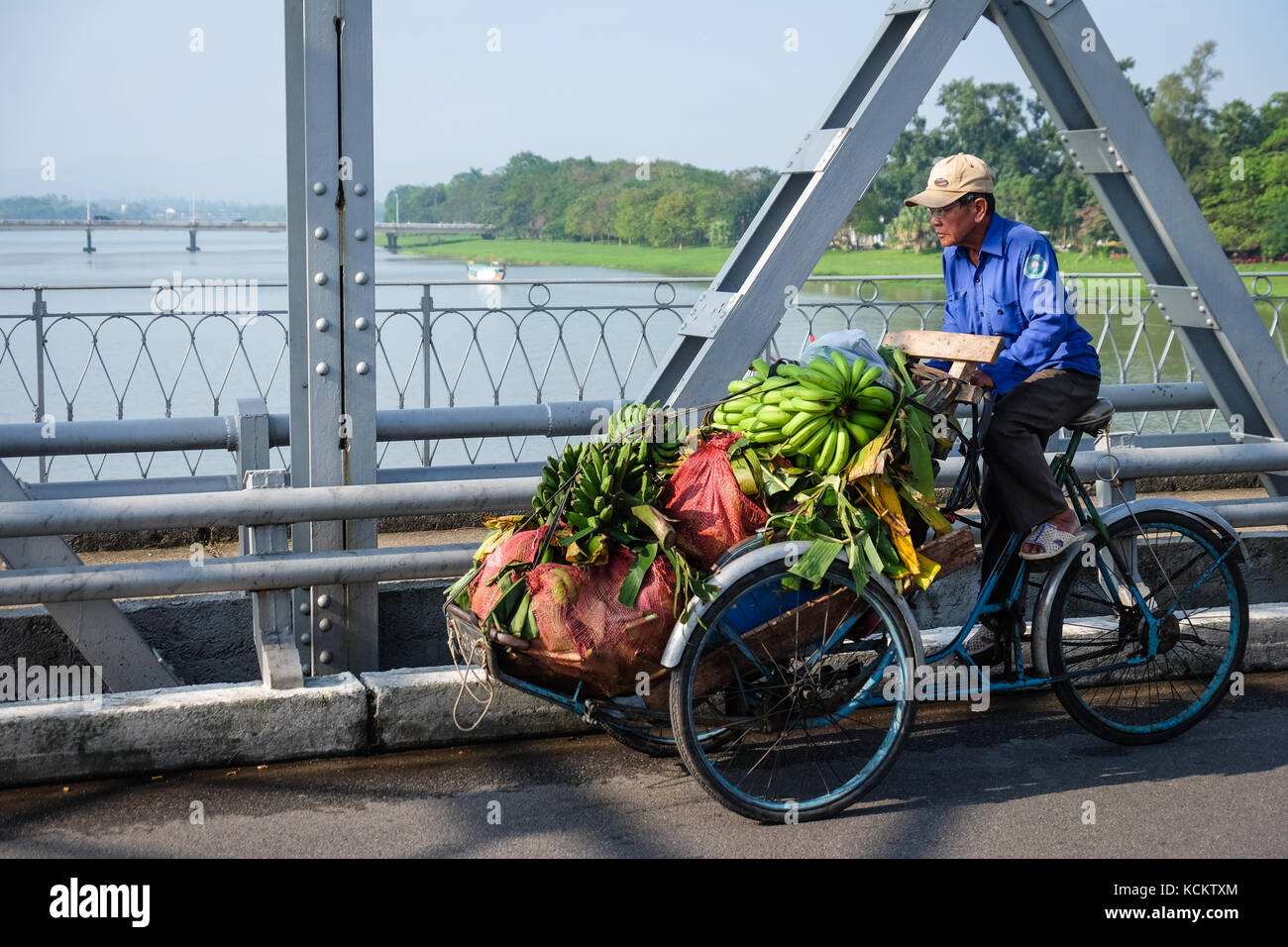 Un uomo in sella alla sua bicicletta laden con banane attraverso Truong Tien Bridge (Cầu Trường Tiền) in tinta. Foto Stock