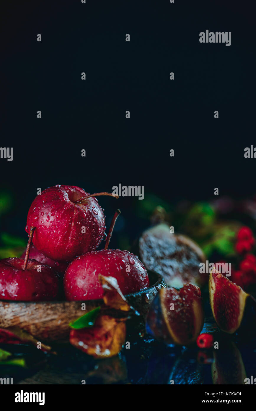 Concetto di raccolto con rossi mele in miniatura di close-up in un autunno ancora in vita con caduta foglie scure della fotografia di cibo con copia spazio. Foto Stock