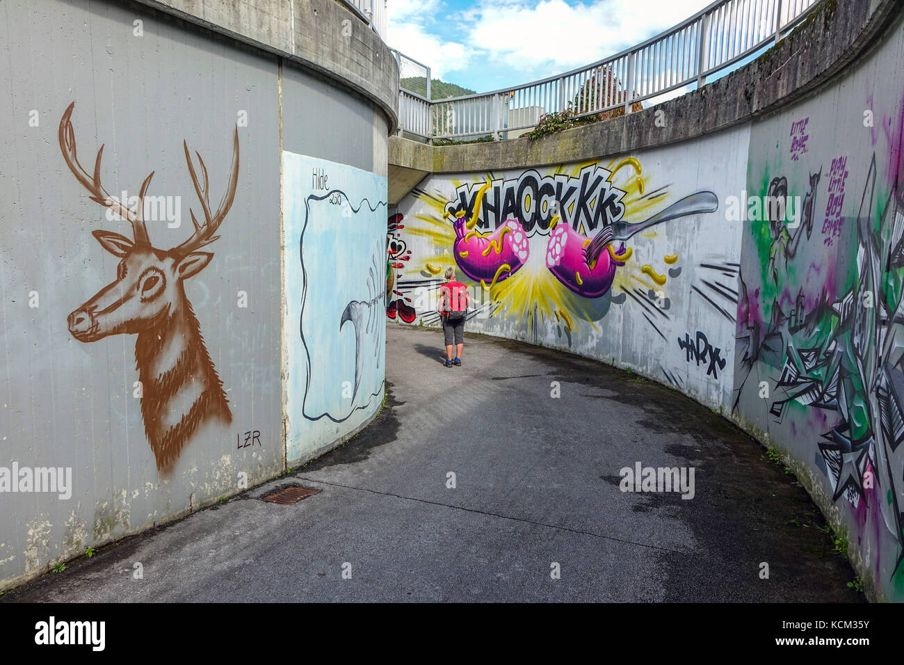 Figura femminile in rosso le passeggiate di fronte all imponente urban graffiti nel sottopasso di calcestruzzo, Austria, Stams, Austria, Foto Stock