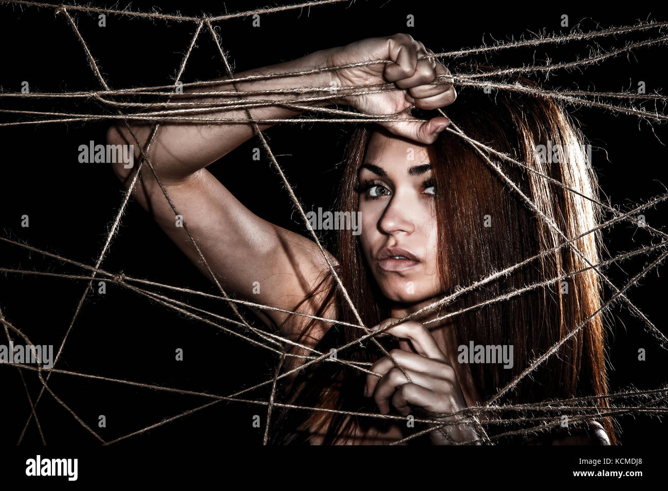 Bella giovane donna dietro le funi interlacciato su sfondo nero Foto Stock