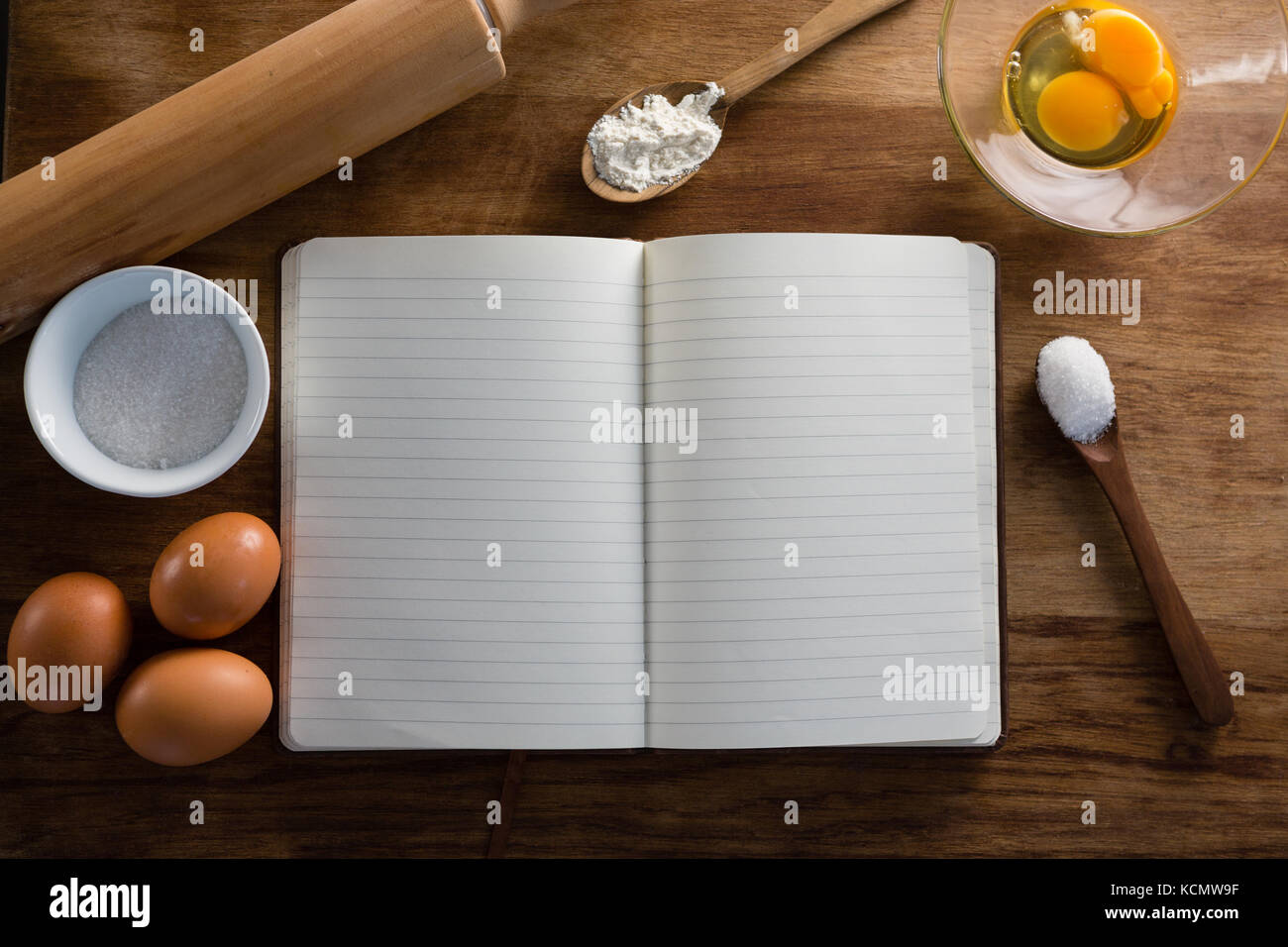 Sopra la testa vista del libro, uova, farina, il cucchiaio e il perno di laminazione mantenuta su un tavolo Foto Stock