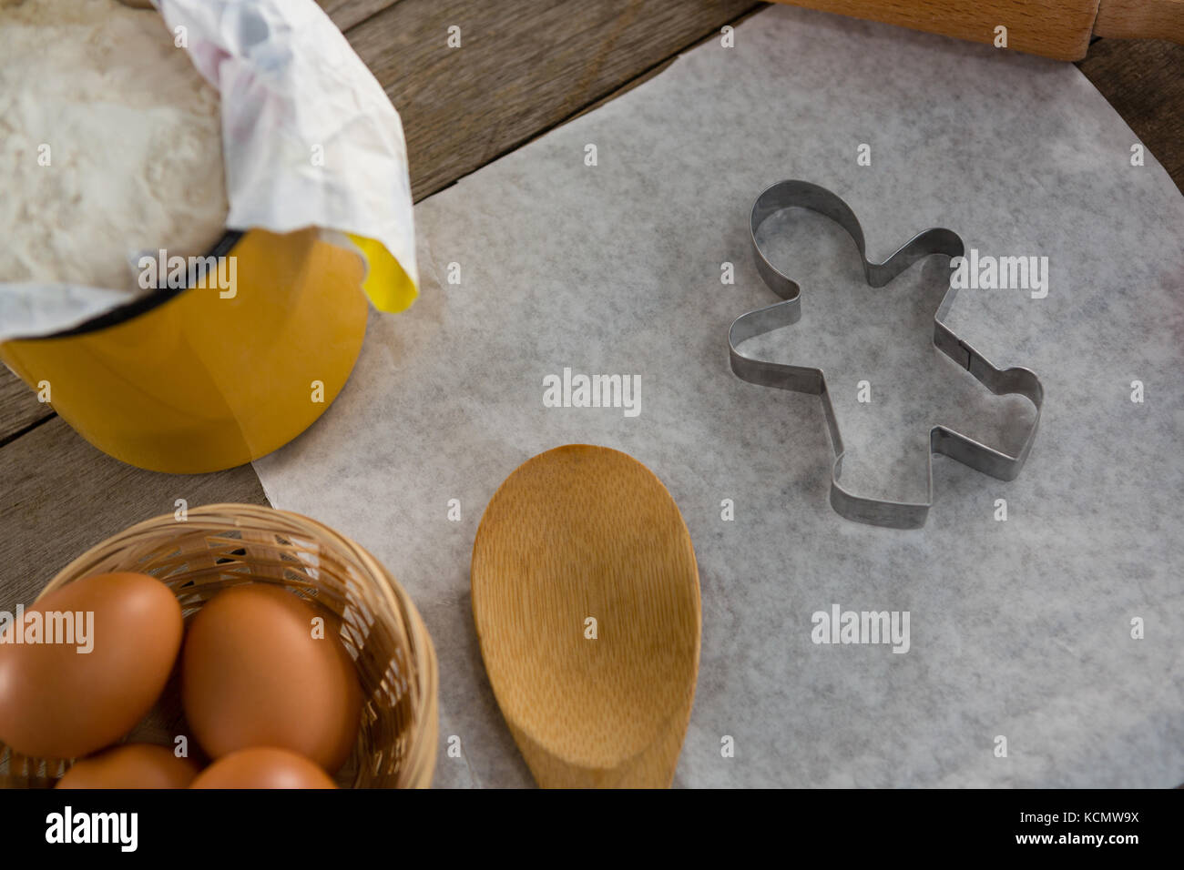 Close-up di carta burro, farina, mattarello cookie cutter e le uova conservate al di sopra di un tavolo di legno Foto Stock