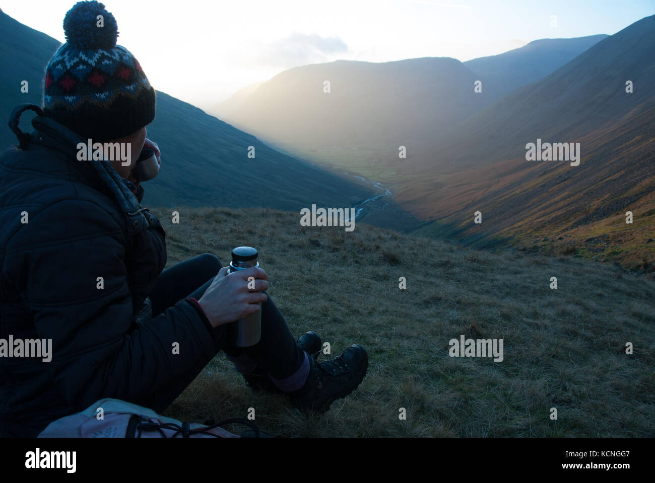 Escursionista in cappello di lana che beve da thermos che guarda giù su Wasdale dalla discesa del grande Gable via Styhead Tarn, Yewbarrow in background, Lago Ditric Foto Stock