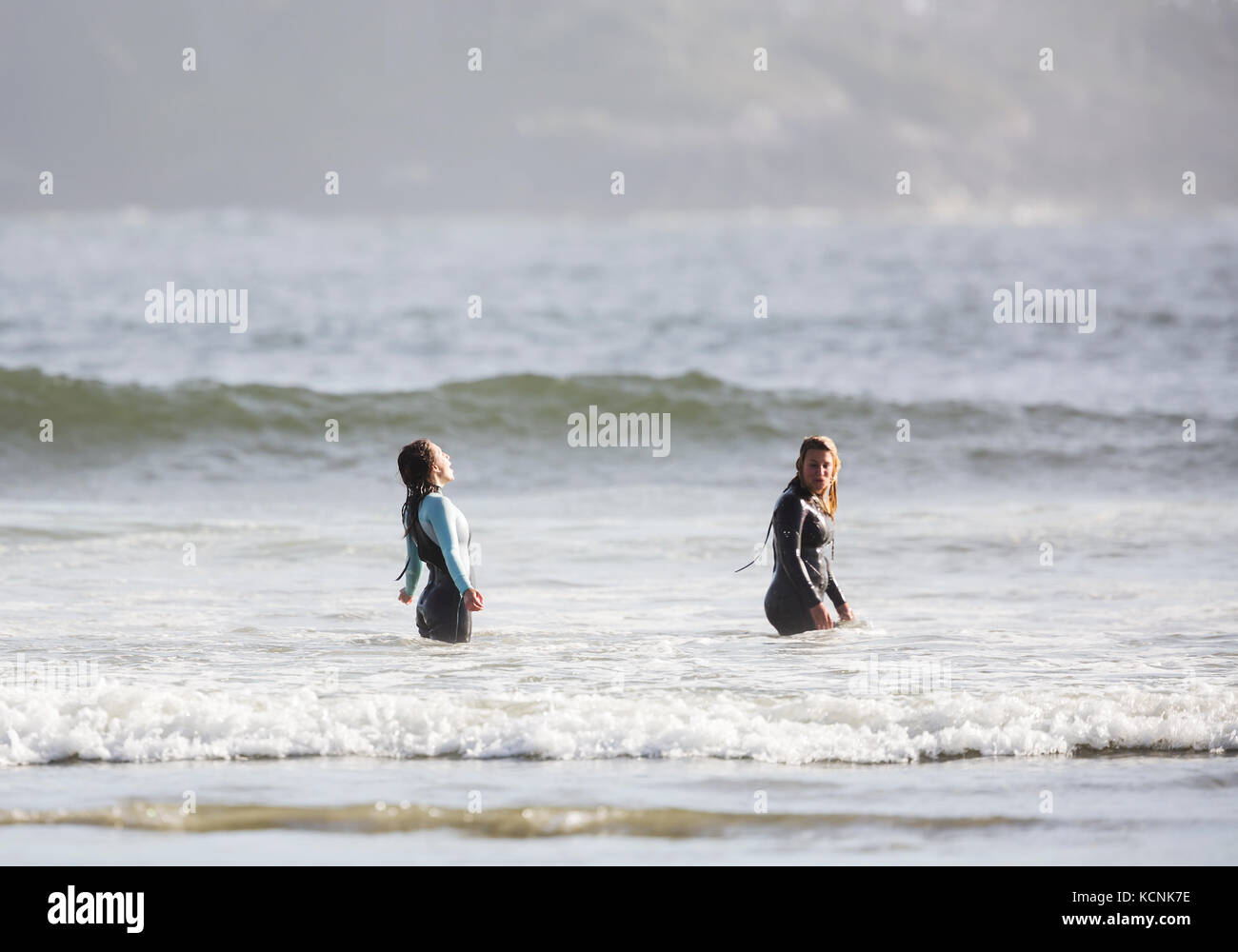 Due amici abbracciare il momento nelle fredde acque del Pacifico, di celebrare un grande giorno di surf off di Chesterman Beach, Tofino, Isola di Vancouver, British Columbia, Canada. Foto Stock