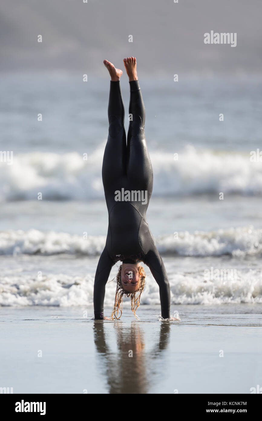 Un surfista femmina si mette in mostra la sua abilità di ginnastica giocando sulla spiaggia di Chesterman. Tofino, Isola di Vancouver, British Columbia, Canada. Foto Stock