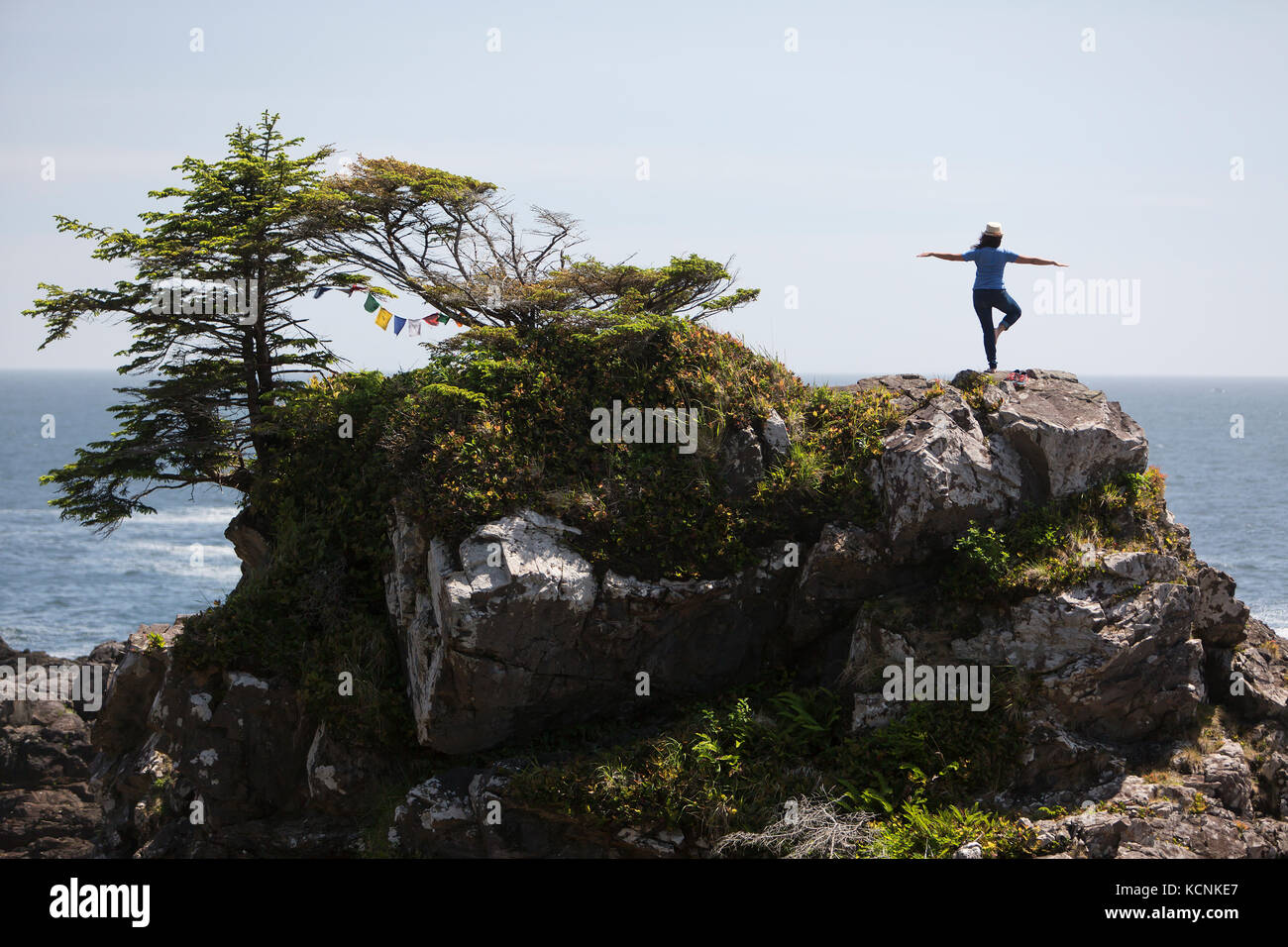 Un visitatore a amphrite faro e pacifico sentiero selvaggio in pratiche ucluelet lei lo yoga e tiene in oceano forma scenica in cima a una roccia che affiora in superficie Foto Stock