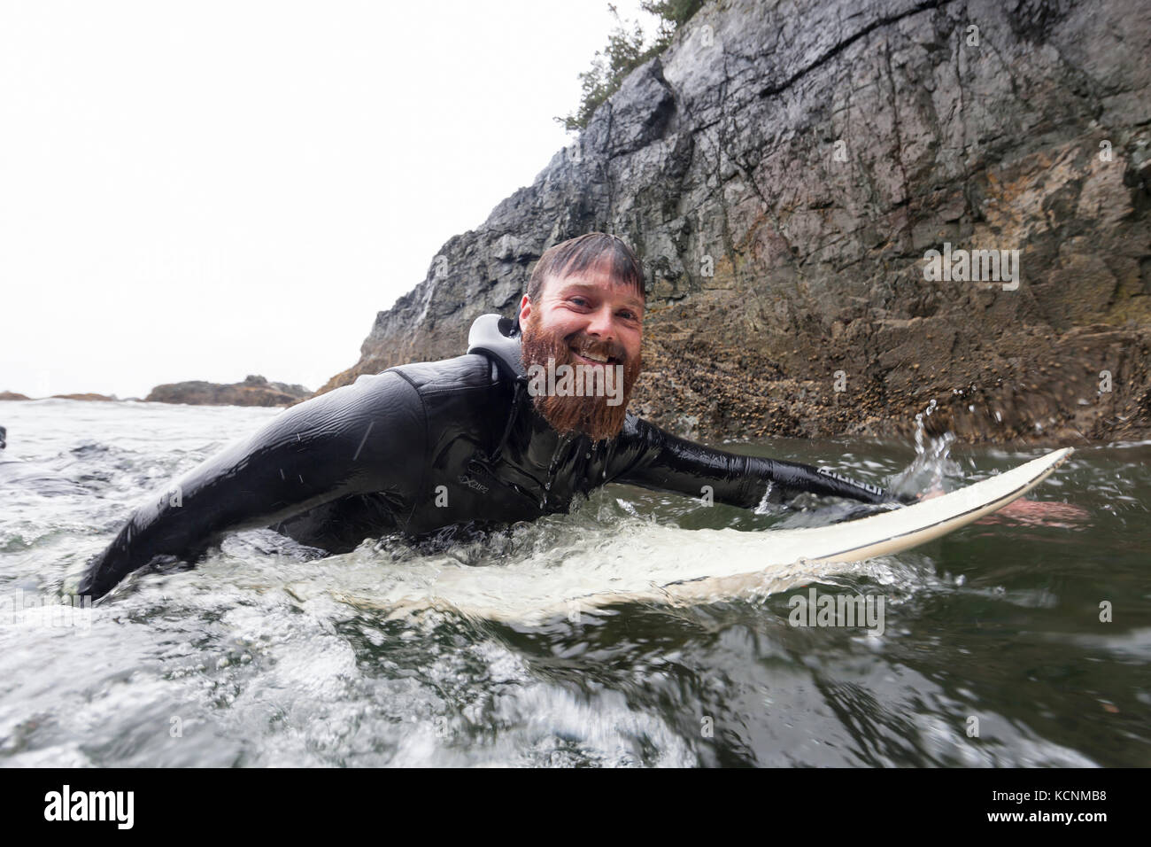 Un surfista nel suo elemento acquoso pagaie nel surf off della molla isola vicino Kyuquot, Isola di Vancouver, British Columbia, Canada. Foto Stock