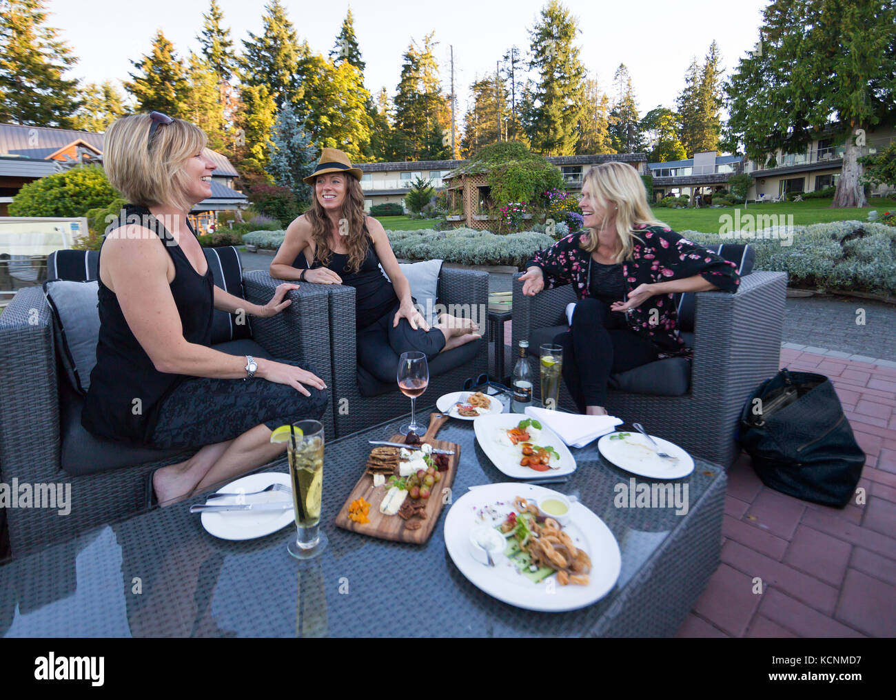 Tre amiche condividono una risata in un patio all'aperto sui terreni del Kingfisher Resort and Spa, courtenay, Vancouver Island, British Columbia, Canada. Foto Stock