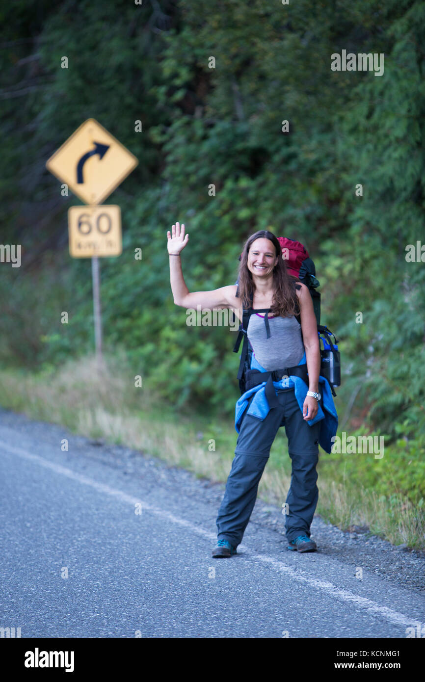 Un hitchhiker sorridente lungo l'autostrada 28 si ondeggia a auto di passaggio sperando di un giro. Strathcona Park, isola di Vancouver. Foto Stock