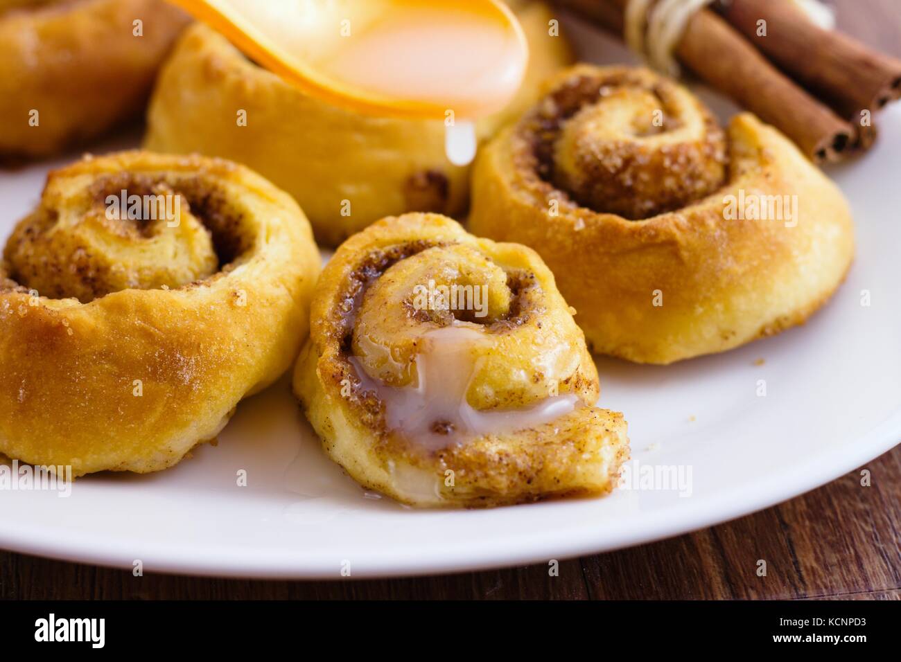 Involtini di cannella tradizionali fatti in casa su piatto bianco ovale con zucchero ricoperto con cucchiaino giallo Foto Stock