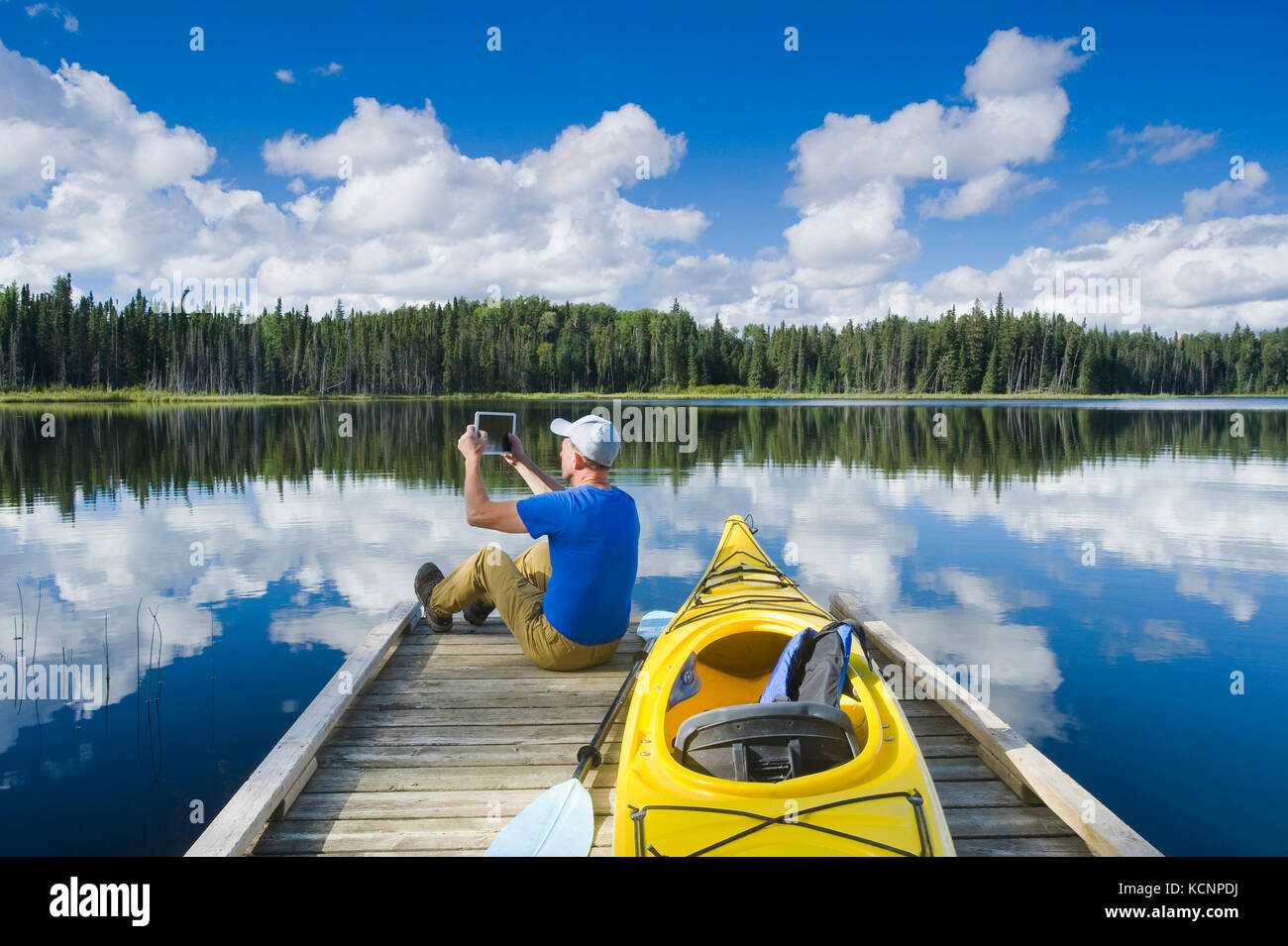 Uomo seduto sul dock accanto al suo kayak mentre utilizzando un tablet, Two Mile Lago , Duck montagna Parco Provinciale, Manitoba, Canada Foto Stock