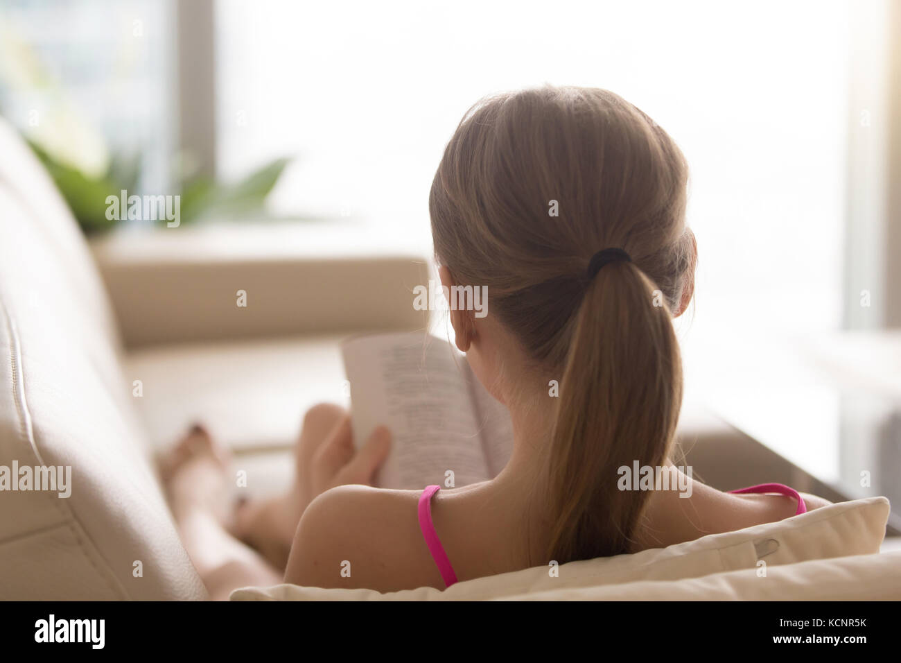 Vista posteriore a donna lettura carta aperto tome sul lettino a casa, giovane amante del libro di trascorrere il tempo libero godendo nuovo romanzo bestseller sul divano, adolescente ri Foto Stock