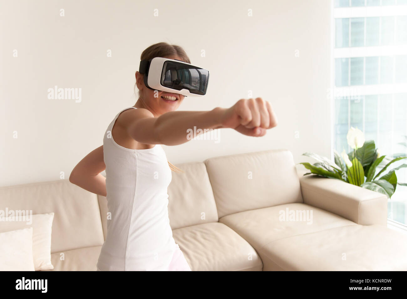 Young Teen gamer che indossa la realtà aumentata bicchieri in piedi in atteggiamento di inscatolamento giocando azione simulatore di gioco mobile app, giocatrice combattimenti con fis Foto Stock