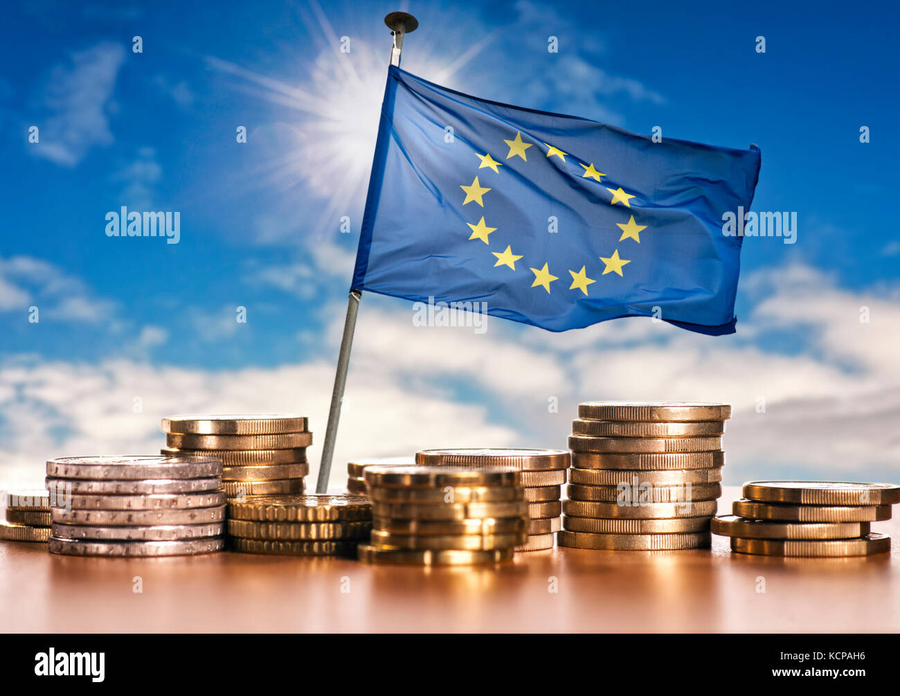 Bandiera europea con pile di monete metalliche in euro nella parte anteriore del cielo blu Foto Stock