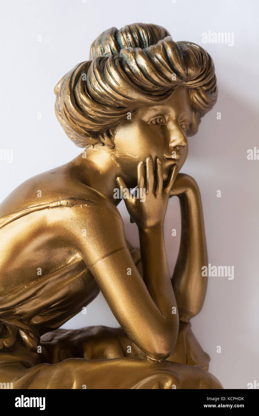 Parte di colore oro ornamento della donna con mento in mani e gomiti appoggiato sulle ginocchia impostato su sfondo bianco Foto Stock