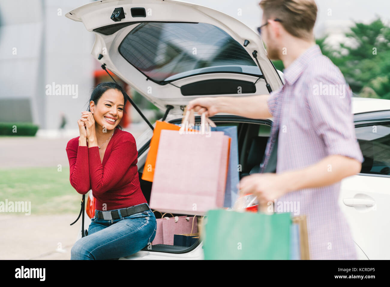 Uomo caucasico fornisce borse per donna asiatica seduta su auto. shopping, amore, multietnica giovane o uno stile di vita informale concetto Foto Stock