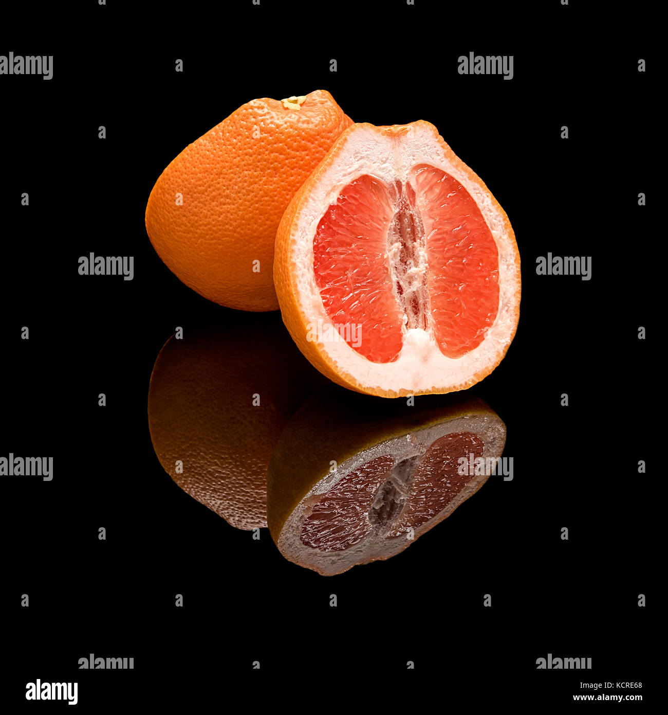 La metà di un pompelmo. Su un lucido nero lo sfondo con una vera riflessione. Foto Stock
