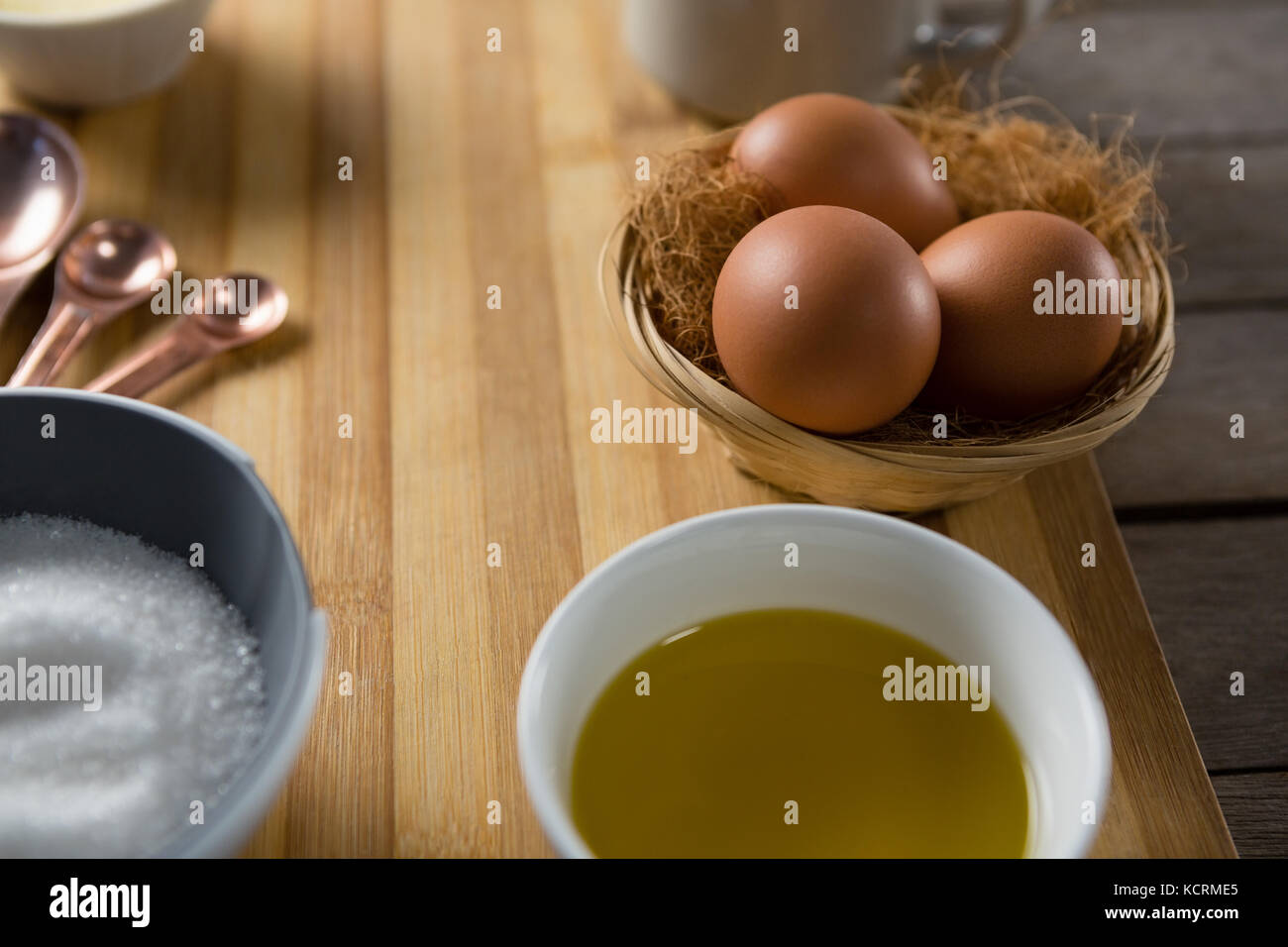 Close-up di uova nel cesto di vimini con olio e zucchero sul pannello di legno Foto Stock