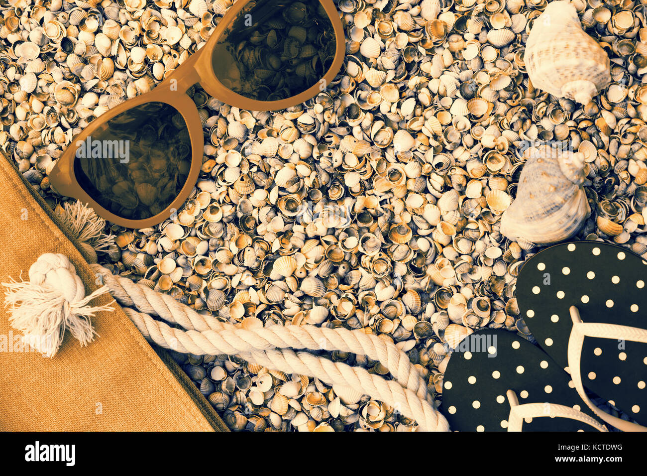 Scena di spiaggia. Accessori donna. Occhiali da sole, flip flop sandali e borsa da spiaggia sdraiato sul mare coquina gusci Foto Stock