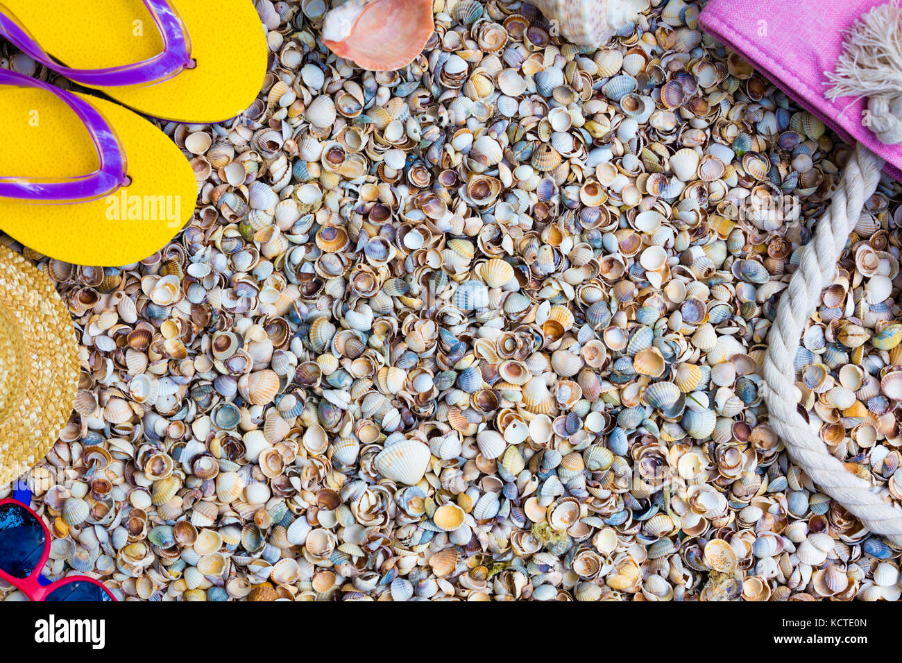 Scena di spiaggia. Accessori donna. Occhiali da sole, flip flop sandali e borsa da spiaggia sdraiato sul mare coquina gusci Foto Stock
