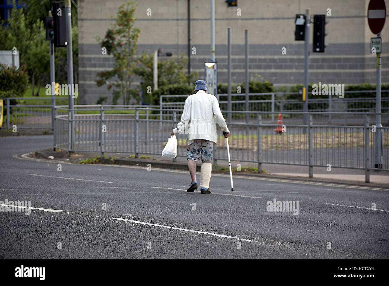 Paziente NHS con bastone da passeggio e gesso che attraversa la strada con pasto da asporto in borsa di trasporto ritorno al Gartnavel General Hospital sera 20:00 Foto Stock