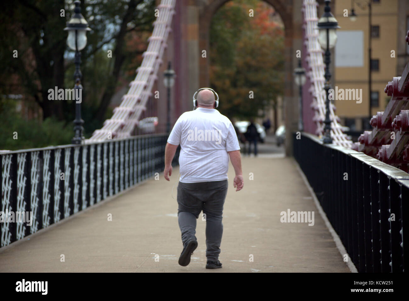 L'uomo maschio ascoltando musica sovrappeso grasso malsano attraversando a piedi il ponte Foto Stock