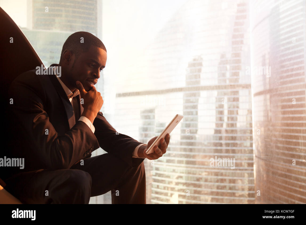 African American businessman utilizzando digitale compressa mentre è seduto in poltrona Egg vicino a finestra con paesaggio urbano fuori. nero ceo la lettura di notizie aziendali Foto Stock