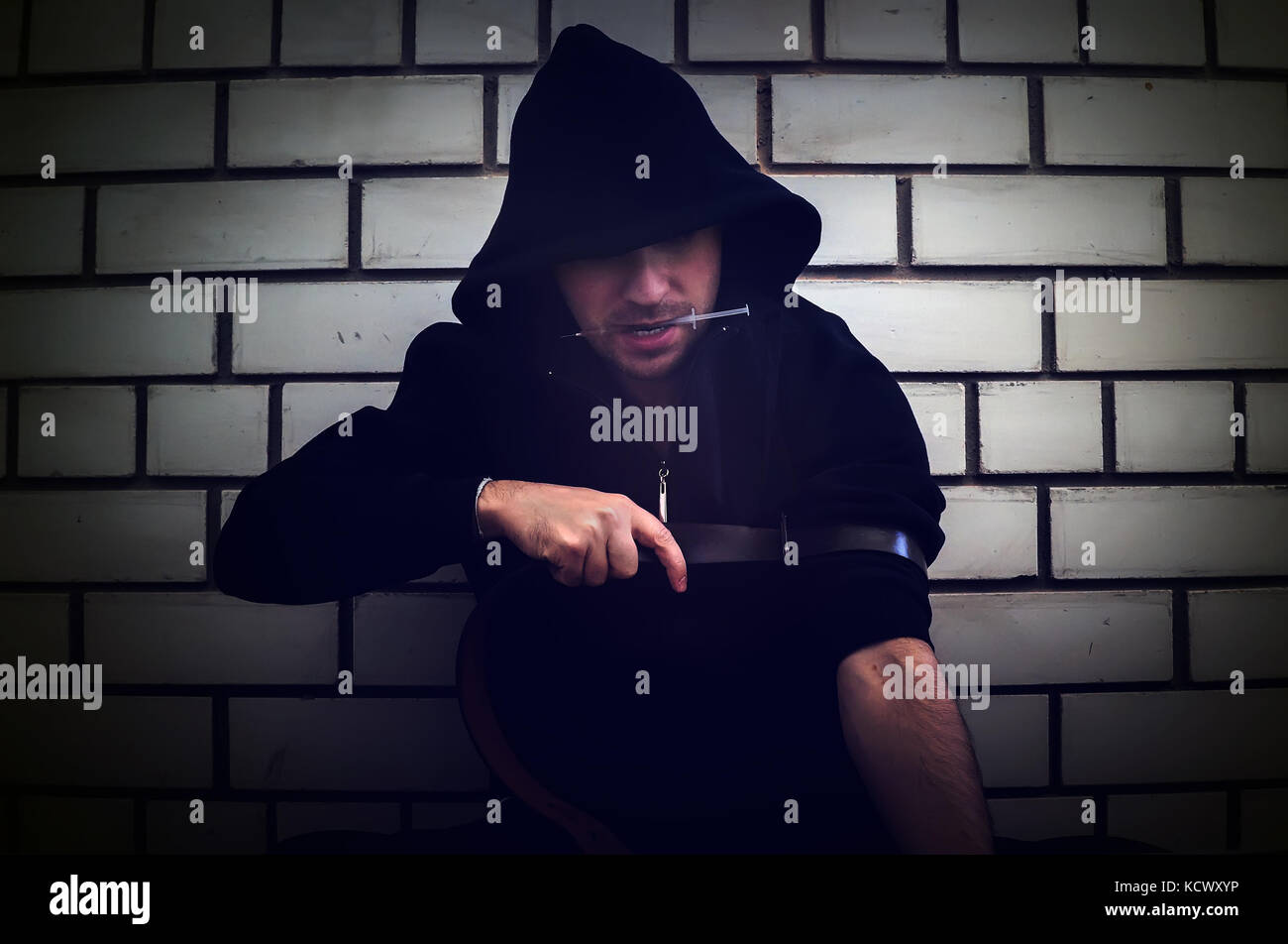 Addict con siringa vuole fare una iniezione in una vena su uno sfondo di un bianco muro di mattoni in un vecchio dirty crack house. Il concetto di dipendenza Foto Stock