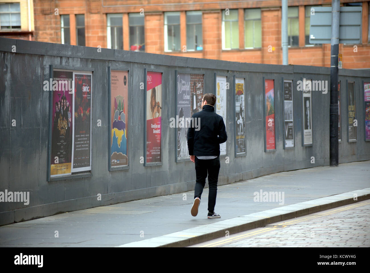 Giovane uomo guardando volare poster sulla strada dal marciapiede visto da dietro nel quartiere di Merchant City Foto Stock