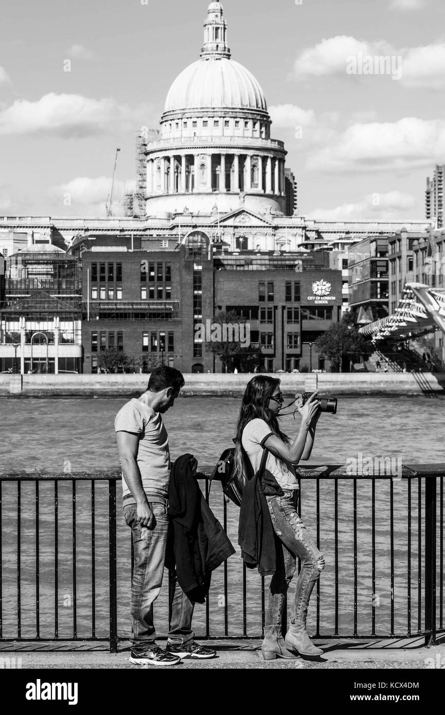 Bianco e nero monocromatico ritratto di una giovane coppia appoggiata contro una recinzione dal fiume Tamigi in bankside southwark Londra indossando cime grigio e b Foto Stock